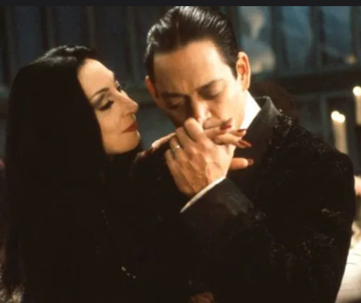 Morticia and Gomez Addams. Gomes is kissing Morticia's hand
